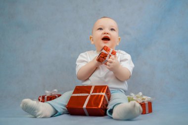 Parlak elbiseli şirin bir erkek bebek mavi bir arka planda oturuyor.