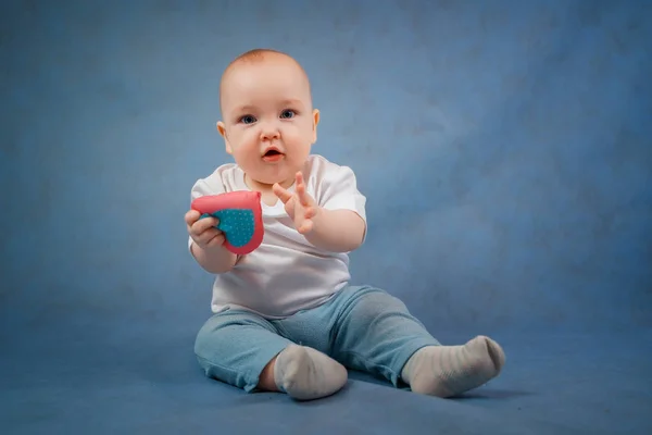 Söt liten bebis i ljusa kläder sitter på en blå bakgrund w — Stockfoto