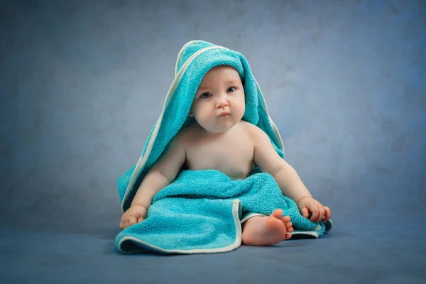 かわいい小さな幼児は床の上の青いタオルで風呂の後に座っています — ストック写真