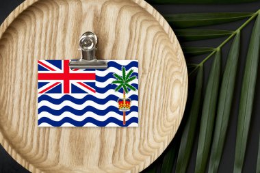 İngiliz Hint Okyanusu Bölgesi bayrağı tahta tabakta işaretlenmiş. Tropik palmiye arka planda canavar bırakır. Asgari ulusal kavram.