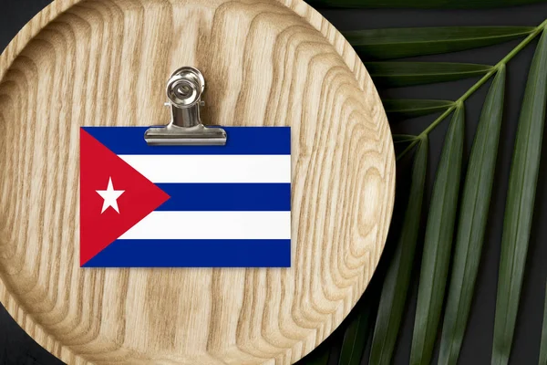 Cuba flag tagged on wooden plate. Tropical palm leaves monstera on background. Minimal national concept.