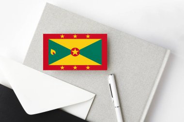 Minimalist arka planda Grenada bayrağı. Beyaz kalemli ve defterli ulusal davetiye zarfı. İletişim konsepti.