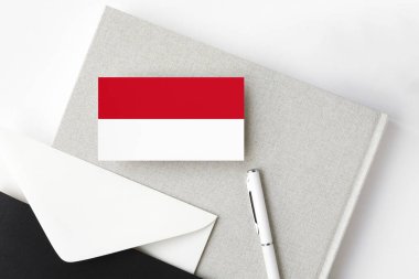 Minimalist arka planda Endonezya bayrağı. Beyaz kalemli ve defterli ulusal davetiye zarfı. İletişim konsepti.
