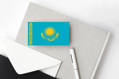 Minimalist harf geçmişinde Kazakistan bayrağı. Beyaz kalemli ve defterli ulusal davetiye zarfı. İletişim konsepti.