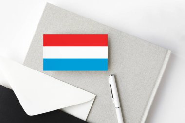 Lüksemburg bayrağı minimalist harf arkaplanında. Beyaz kalemli ve defterli ulusal davetiye zarfı. İletişim konsepti.