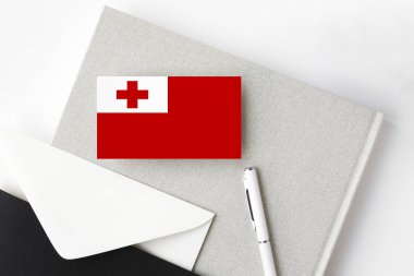 Minimalist arka planda Tonga bayrağı. Beyaz kalemli ve defterli ulusal davetiye zarfı. İletişim konsepti.