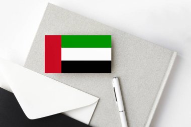 Birleşik Arap Emirlikleri bayrağı minimalist harf arkaplanında. Beyaz kalemli ve defterli ulusal davetiye zarfı. İletişim konsepti.