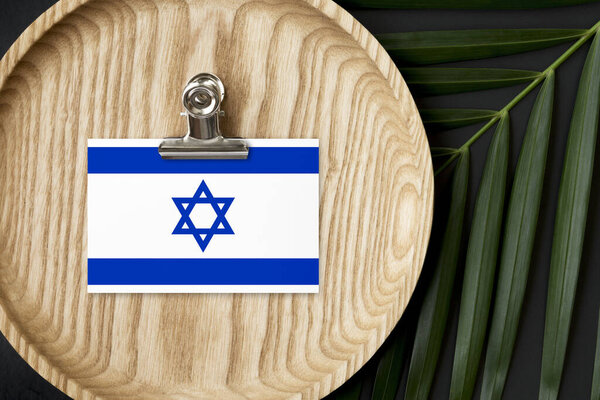 Israel flag tagged on wooden plate. Tropical palm leaves monstera on background. Minimal national concept.