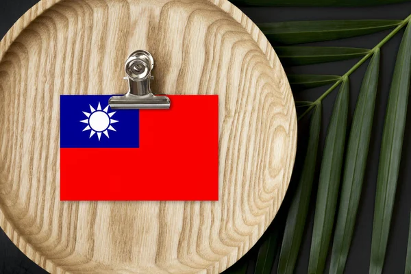Taiwan flag tagged on wooden plate. Tropical palm leaves monstera on background. Minimal national concept.