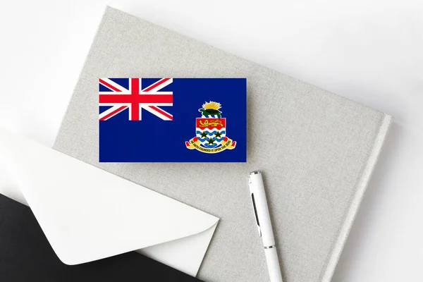 开曼群岛的国旗以简约字母为背景 有白色钢笔和笔记本的国家邀请函 传播概念 — 图库照片