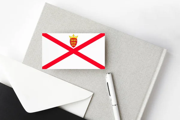 Jersey flag on minimalist letter background. National invitation envelope with white pen and notebook. Communication concept.