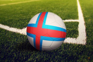 Faroe Adaları topu köşeye sıkıştırdı, futbol sahası arka planında. Ulusal futbol teması yeşil çimlerde.