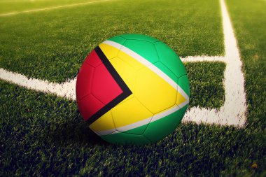 Topun üzerinde Guyana bayrağı, köşe vuruşu pozisyonu, futbol sahası arka planı. Ulusal futbol teması yeşil çimlerde.
