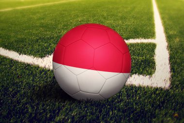 Köşede top üzerinde Monako bayrağı, futbol sahasında arka plan. Ulusal futbol teması yeşil çimlerde.