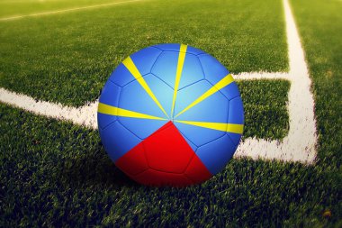 Topun üzerinde yeniden birleşme bayrağı, köşe vuruşu pozisyonu, futbol sahasında arka plan. Ulusal futbol teması yeşil çimlerde.