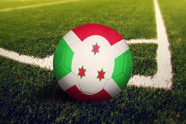 Burundi flag on ball at corner kick position, soccer field background. National football theme on green grass.