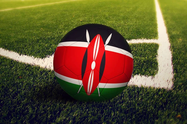 Kenya flag on ball at corner kick position, soccer field background. National football theme on green grass.