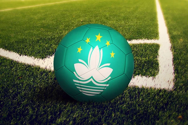 Macao flag on ball at corner kick position, soccer field background. National football theme on green grass.