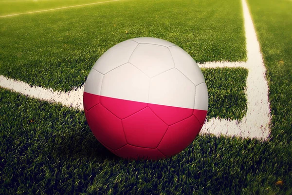 Poland flag on ball at corner kick position, soccer field background. National football theme on green grass.