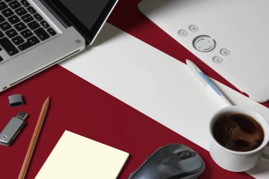 Üst görünümde Letonya ulusal bayrağı dizüstü bilgisayarı, klavyesi, usb sürücüsü, grafik tableti, kahve fincanı, ahşap masadaki fare yaratıcı tasarımcının çalışma alanı.