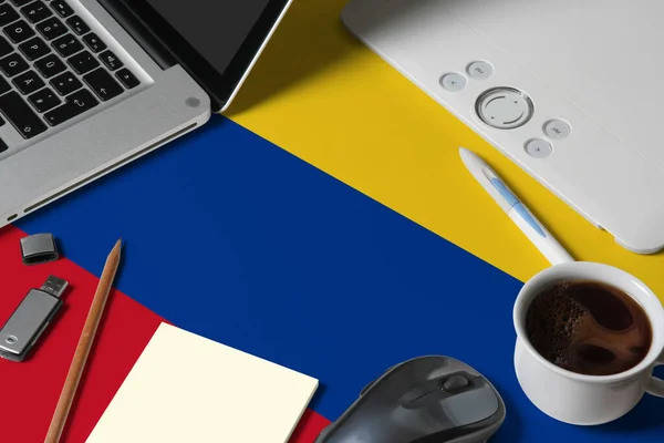 Colombia national flag on top view work space of creative designer with laptop, computer keyboard, usb drive, graphic tablet, coffee cup, mouse on wooden table.