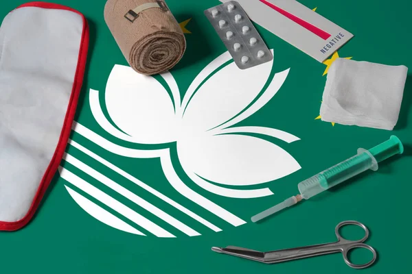 Macao flag with first aid medical kit on wooden table background. National healthcare system concept, medical theme.