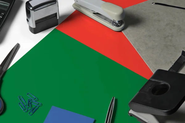 Madagascar flag with office clerk workplace background. National stationary concept with office tools.