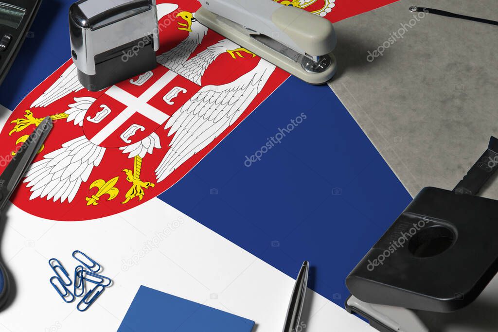 Serbia flag with office clerk workplace background. National stationary concept with office tools.