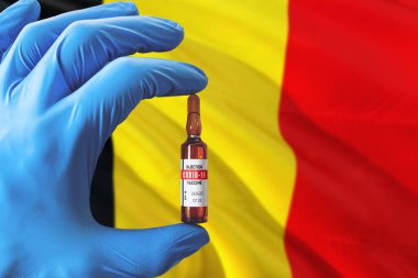 Coronavirus Covid-19 konseptli Belçika bayrağı. Mavi koruma eldivenli doktor elinde aşı şişesi tutuyor. Salgın virüsü, Cov-19, Corona virüsü salgını.