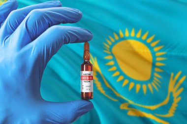 Coronavirus Covid-19 konseptli Kazakistan bayrağı. Mavi koruma eldivenli doktor elinde aşı şişesi tutuyor. Salgın virüsü, Cov-19, Corona virüsü salgını.