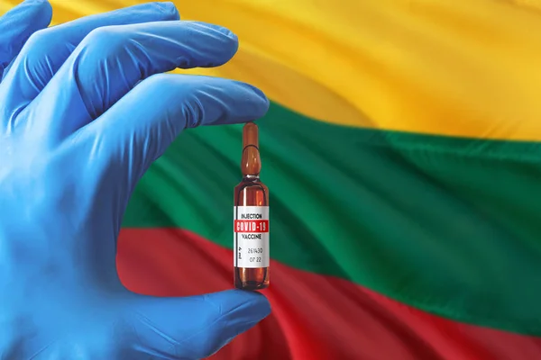 Lithuania flag with Coronavirus Covid-19 concept. Doctor with blue protection medical gloves holding a vaccine bottle. Epidemic Virus, Cov-19, Corona virus outbreaking.