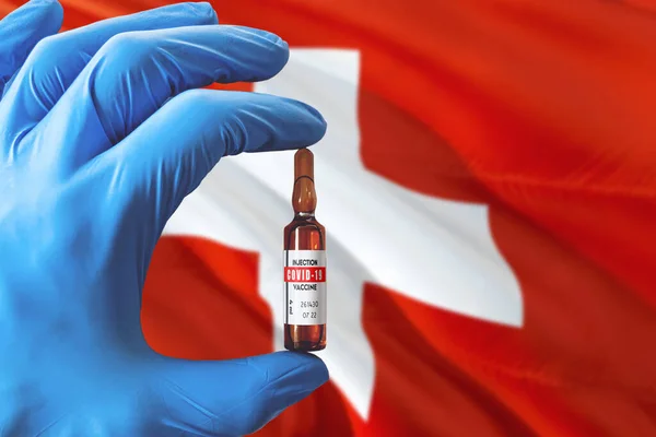 Switzerland flag with Coronavirus Covid-19 concept. Doctor with blue protection medical gloves holding a vaccine bottle. Epidemic Virus, Cov-19, Corona virus outbreaking.