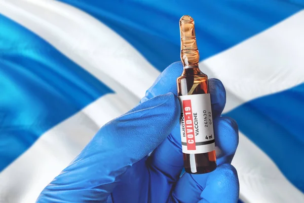 Scotland flag with Coronavirus Covid-19 concept. Doctor with blue protection medical gloves holds a vaccine bottle. coronavirus covid 19 vaccine research.