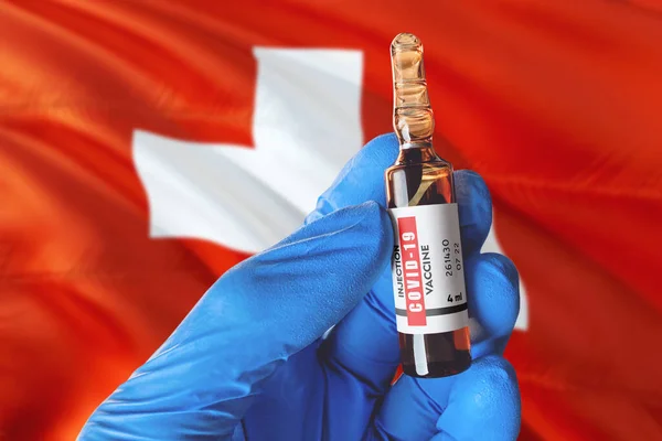 Switzerland flag with Coronavirus Covid-19 concept. Doctor with blue protection medical gloves holds a vaccine bottle. coronavirus covid 19 vaccine research.