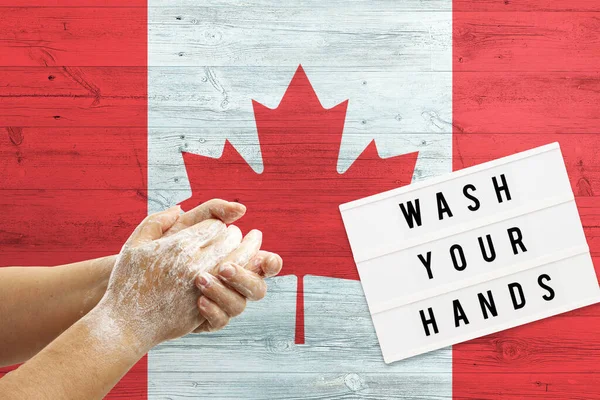 Canada flag background on wooden surface. Minimal wash your hands board with minimal international hygiene concept hand detail.