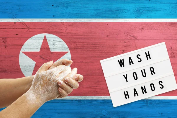 North Korea flag background on wooden surface. Minimal wash your hands board with minimal international hygiene concept hand detail.