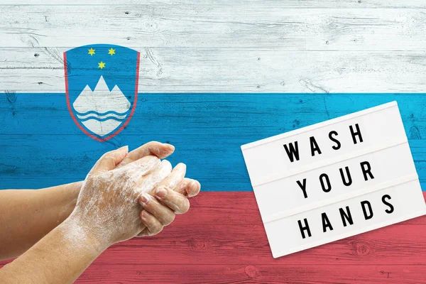 Slovenia flag background on wooden surface. Minimal wash your hands board with minimal international hygiene concept hand detail.