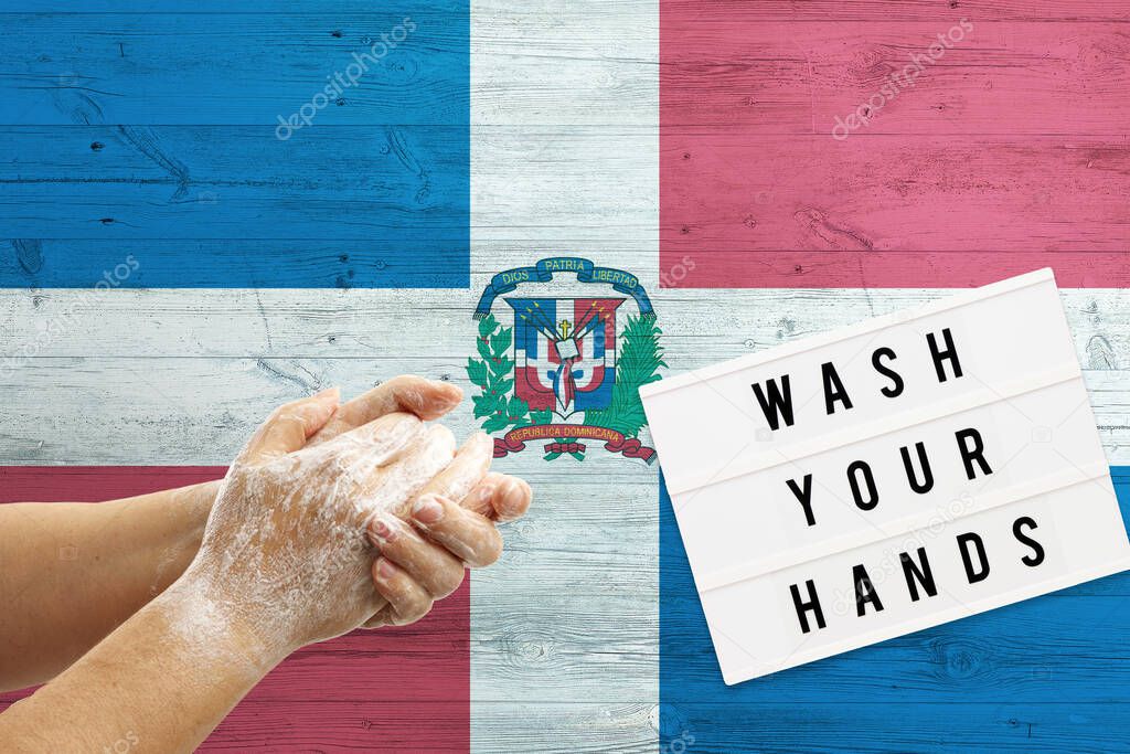 Dominican Republic flag background on wooden surface. Minimal wash your hands board with minimal international hygiene concept hand detail.