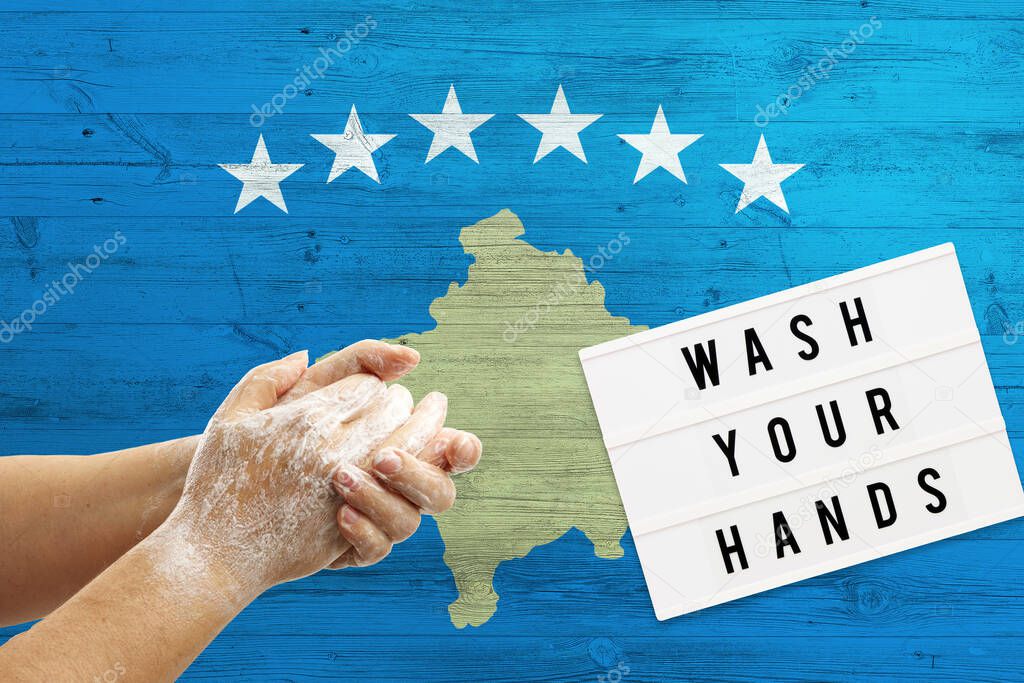 Kosovo flag background on wooden surface. Minimal wash your hands board with minimal international hygiene concept hand detail.