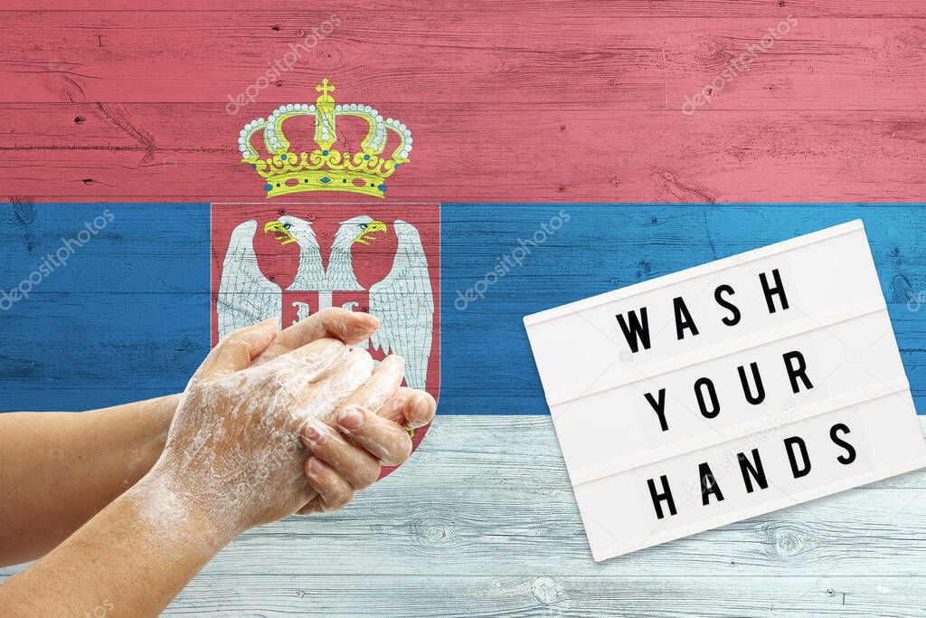 Serbia flag background on wooden surface. Minimal wash your hands board with minimal international hygiene concept hand detail.