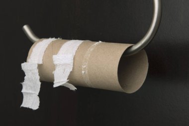 Siyah bir duvara karşı boş bir tuvalet kağıdı rulosu..