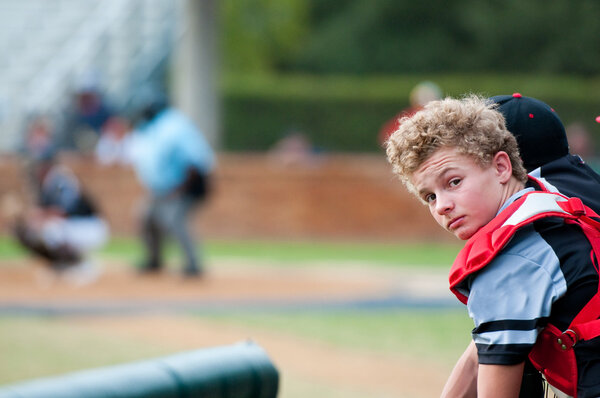 Baseball catcher leaning over dugout fence looking at camera.