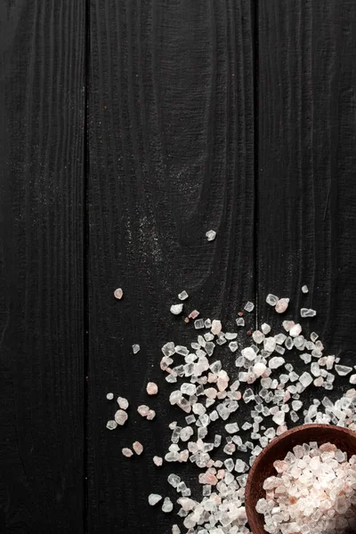 一片粉红色的喜马拉雅山盐散落在黑色的木制背景上。屏幕角上有一碗盐.登记的地方 — 图库照片