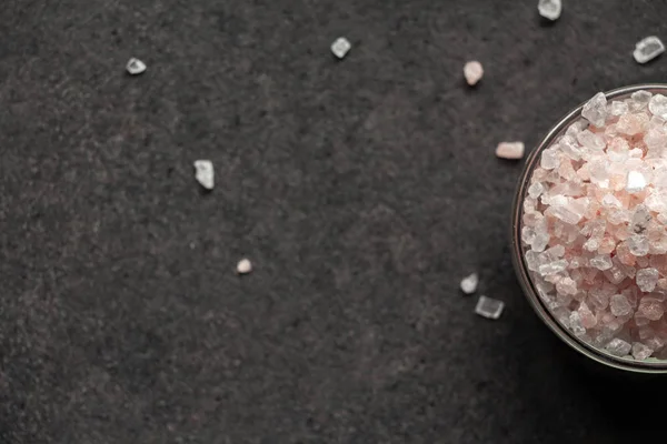 Spilled salt near a saucer full of Himalayan salt on a black slate board.With place for inscription.