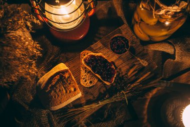Ahşap bir tahtanın üzerinde mum ışığında reçelli dilimlenmiş ekmek. Kırsal atmosfer. Fotoğraf üstten.