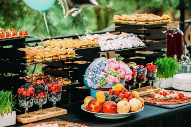 Çeşitli atıştırmalıklar ve dilimlerle dolu bir masa. Açık hava partisinde yemek. Mini burgerler ve kanepeler. Yemek çiçekleri ve otlarla süslenmiş bir masa..