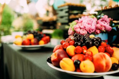Açık hava partisinde çiçeklerle süslenmiş bir masada meyve tabağı..