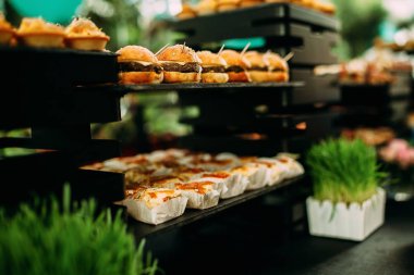 Bayram masasında mini burgerler ve kanepeler. Açık hava partisinde güzel dekore edilmiş çimenler ve çiçeklerle dolu bir masa.