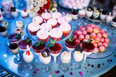 Farklı kek ve tatlılarla süslenmiş güzel bir masa. Reçelli dondurma ve bardakta nane şekeri. Meyveli kanepeler. Pembe biberli büyük bir tabak. Pembe şekerli kavanoz. Meyveli hurma.