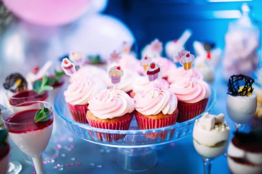 Farklı kek ve tatlılarla süslenmiş güzel bir masa. Neon mavi ışıkta pembe çörekler, reçelli çikolata ve naneli dondurma. Bir çocuğun doğum gününde tatlılar.